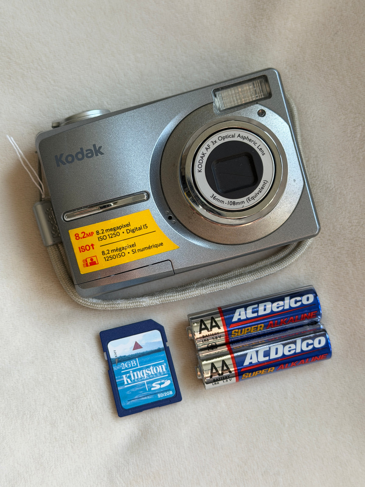 Kodak EasyShare C813 digital camera in gray with batteries and memory card laid flat