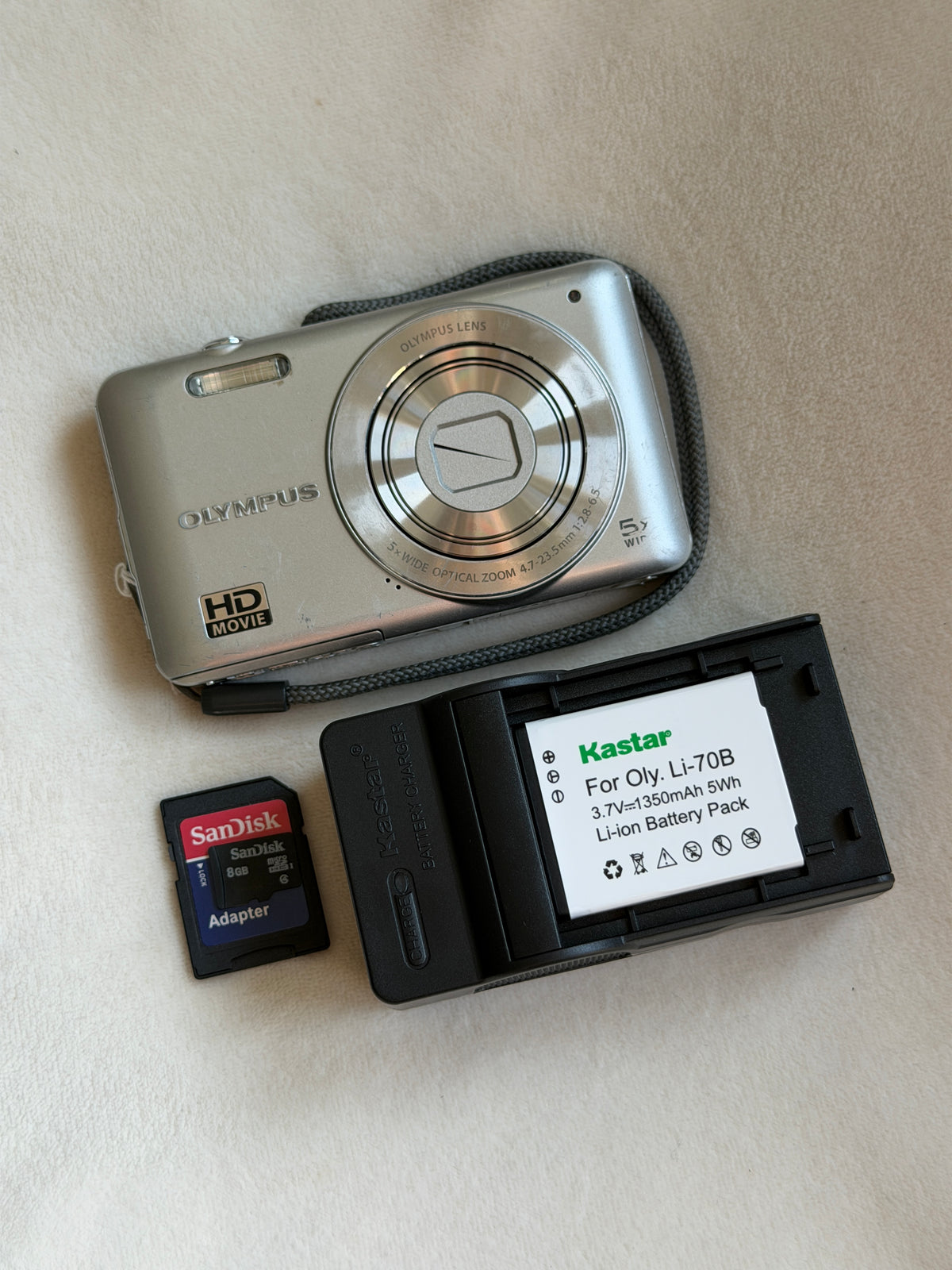 Olympus VG-120 digital camera in silver with battery, charger and memory card laid flat