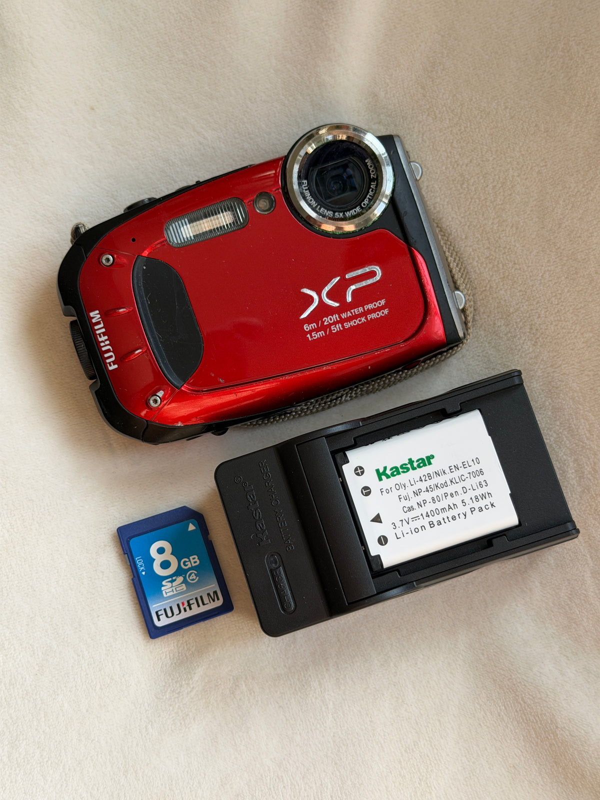 Fujifilm FinePix XP60 waterproof digital camera in red with battery, charger and memory card laid flat