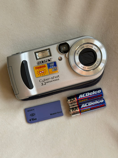 Sony Cyber-shot DSC-P71 digital camera in silver with batteries and Memory Stick laid flat
