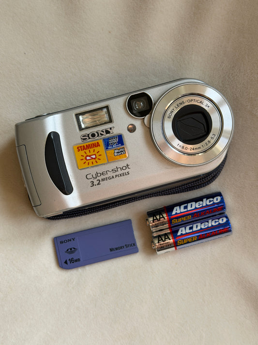 Sony Cyber-shot DSC-P71 digital camera in silver with batteries and Memory Stick laid flat