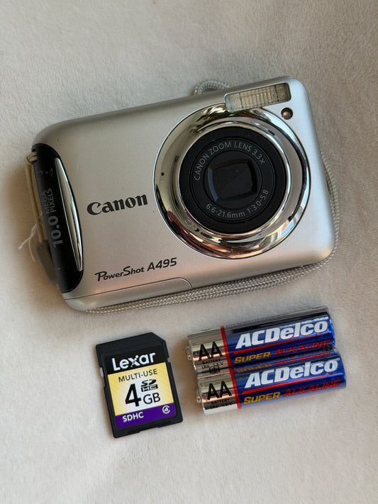 Canon PowerShot A495 digital camera in silver with batteries and memory card laid flat
