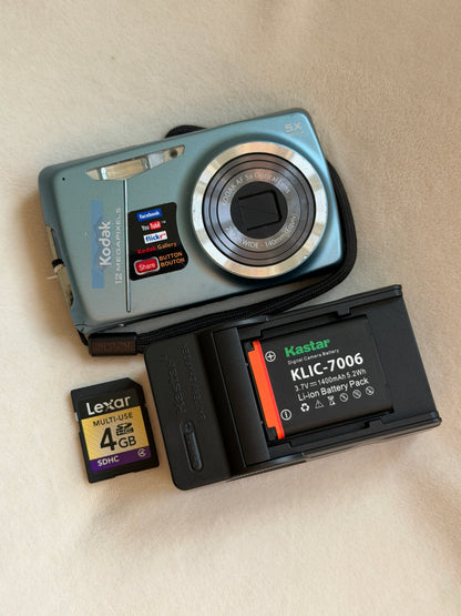 Kodak EasyShare M550 digital camera in blue with battery, charger and memory card laid flat
