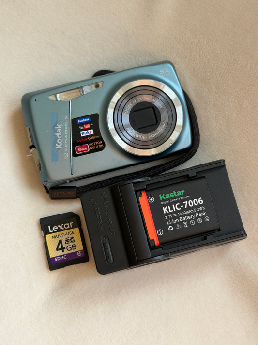 Kodak EasyShare M550 digital camera in blue with battery, charger and memory card laid flat