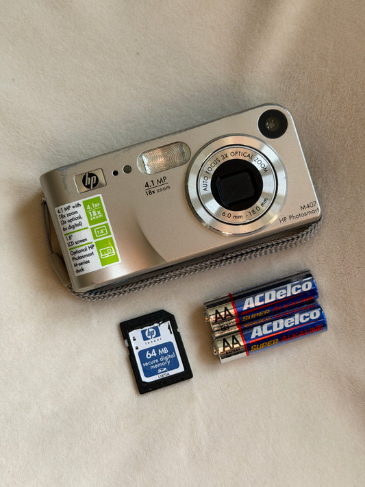 HP Photosmart M407 digital camera in silver with batteries and memory card laid flat