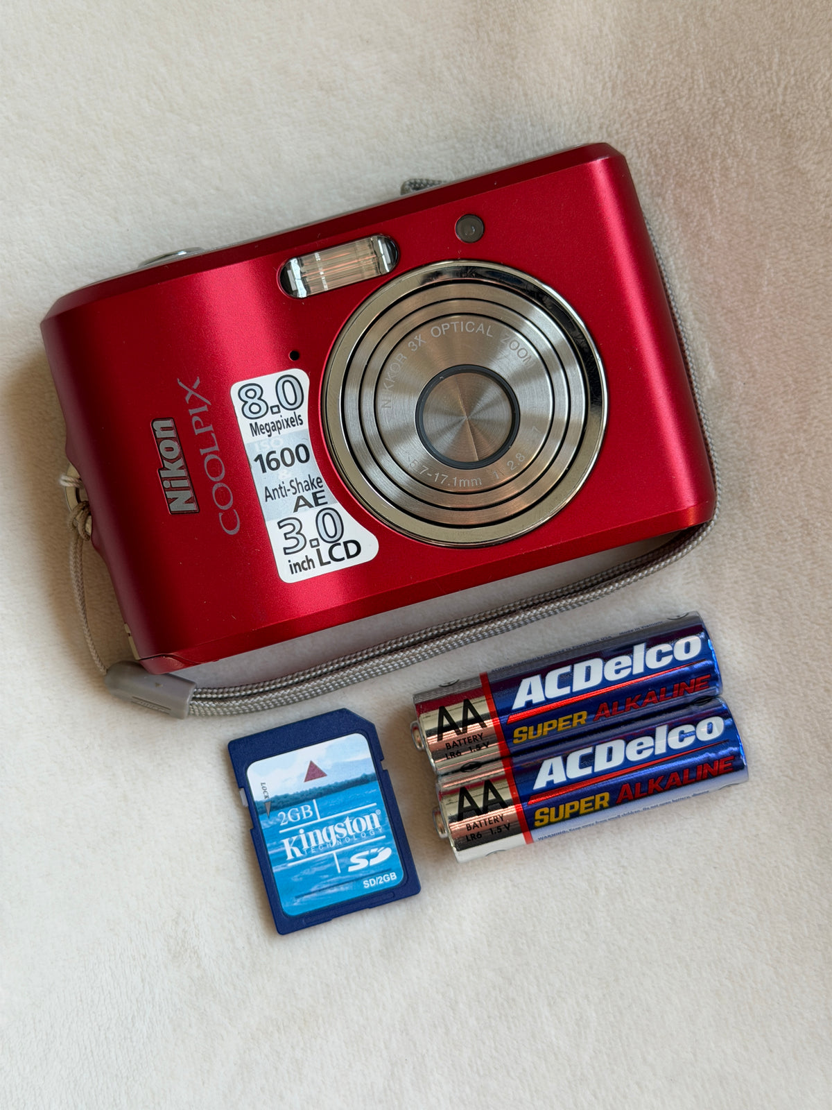 Nikon Coolpix L18 digital camera in red with batteries and memory card laid flat