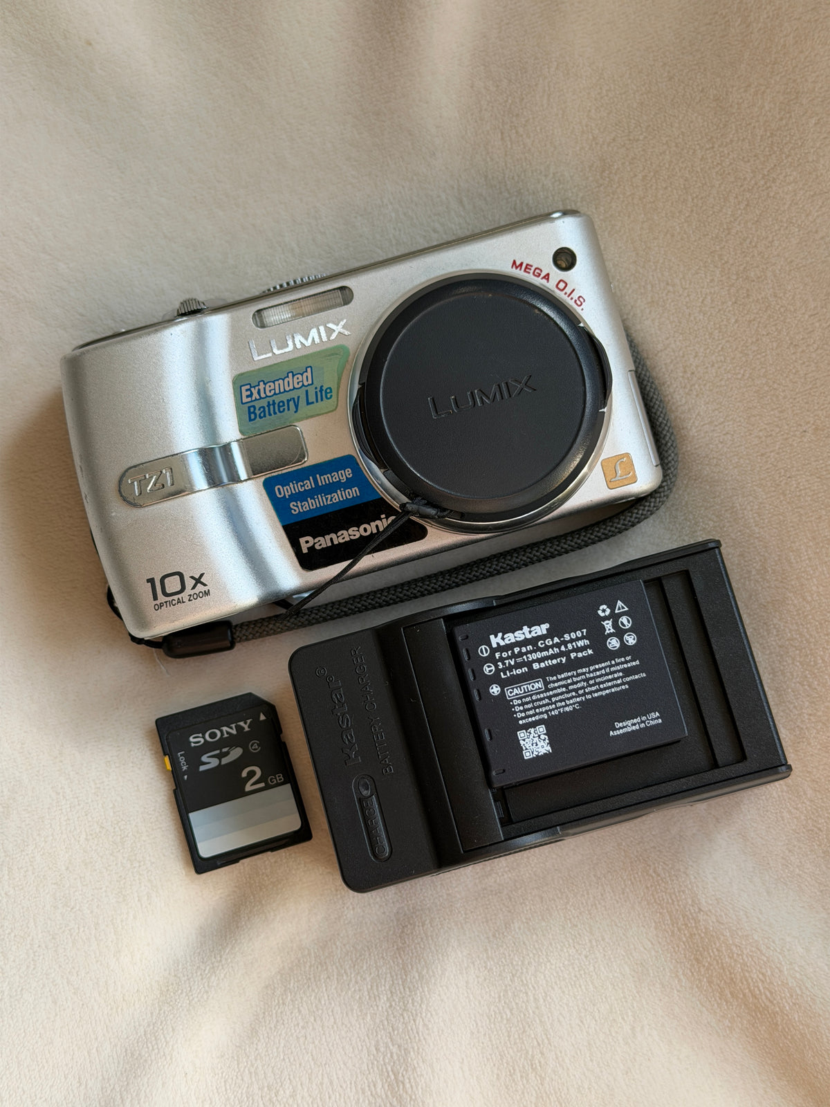 Panasonic Lumix DMC-TZ1 digital camera in silver with battery, charger and memory card laid flat