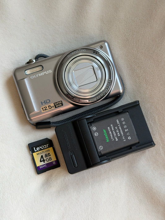 Olympus VR-320 digital camera in silver with battery, charger and memory card laid flat